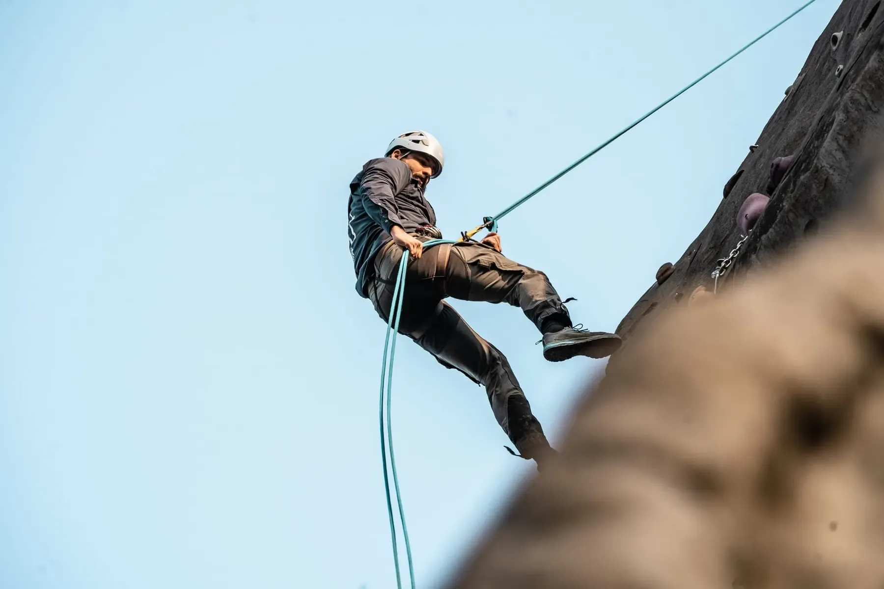 Een abseiler laat zich langs de rotswand zakken tegen een strakblauwe lucht