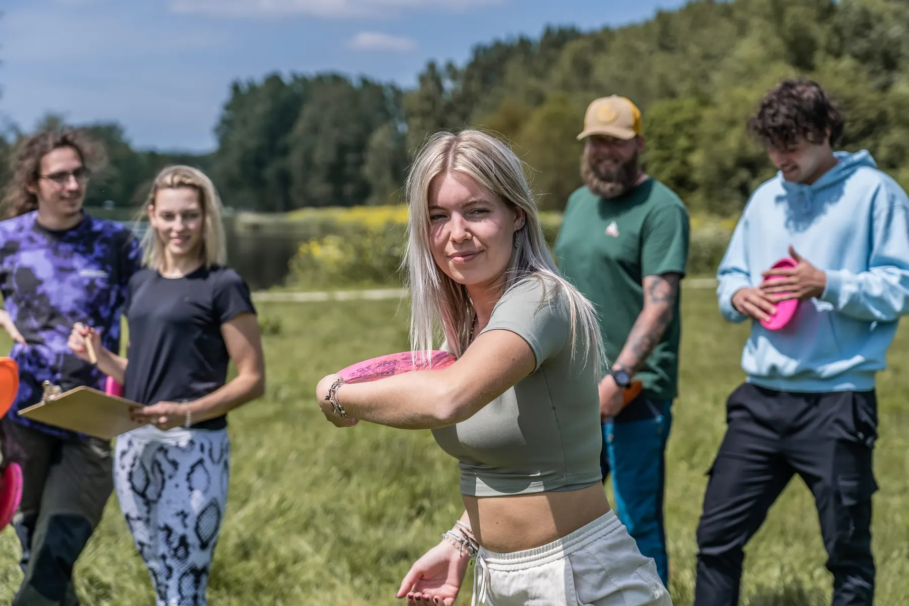 Een deelneemster haalt uit om haar disc te werpen, de groep kijkt toe