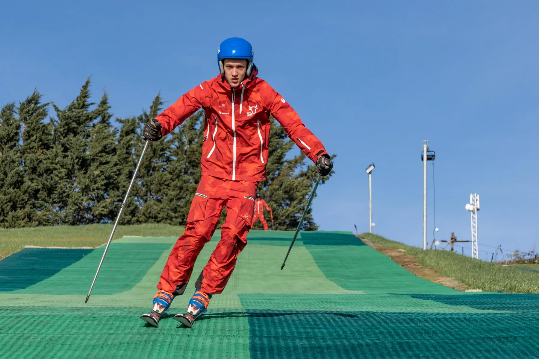 Een skiër in rood skipak op de groene skimatten van de outdoor skibaan
