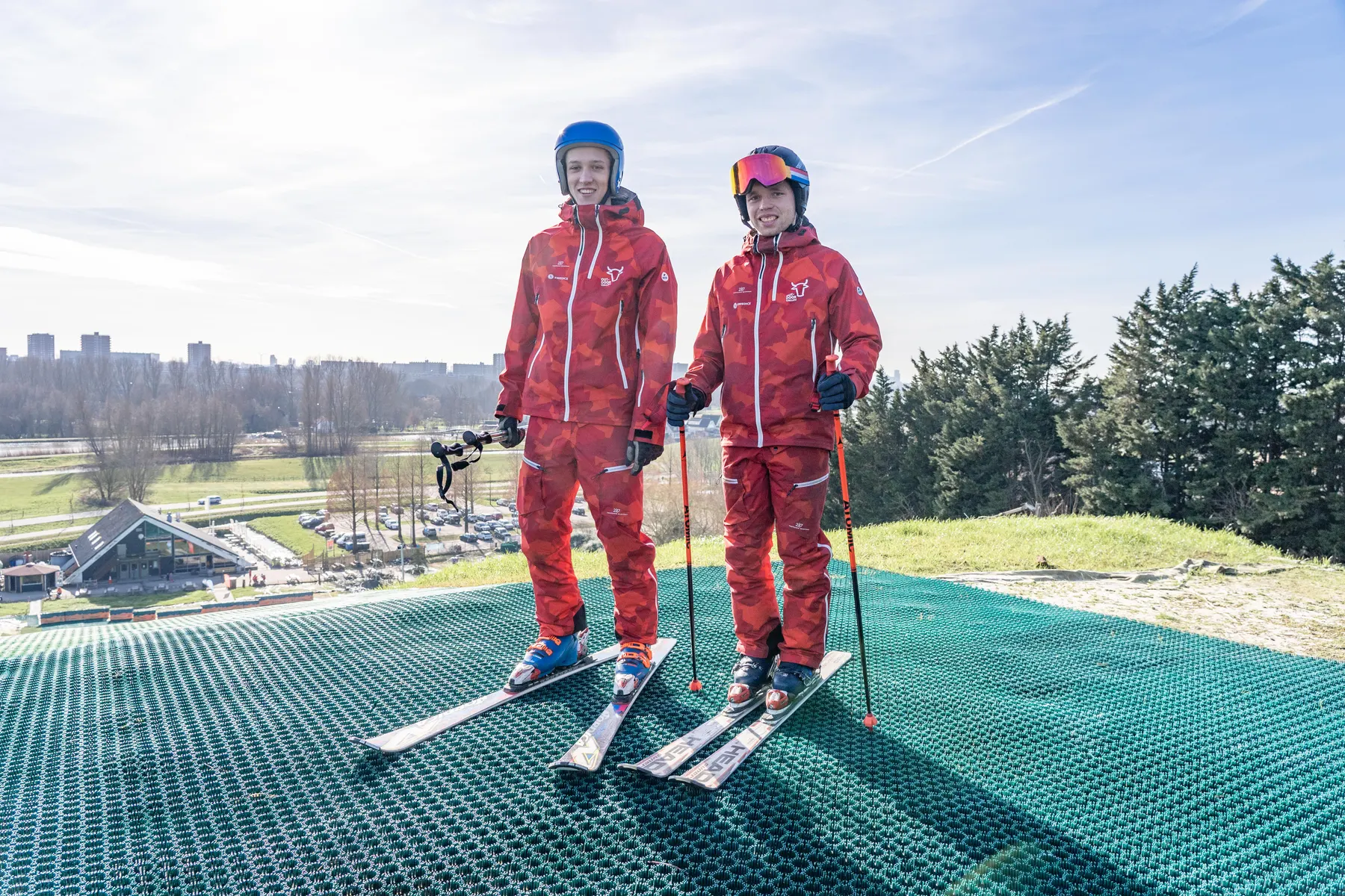 Twee skiërs in skipak met helm en skibril bovenaan de outdoor skibaan
