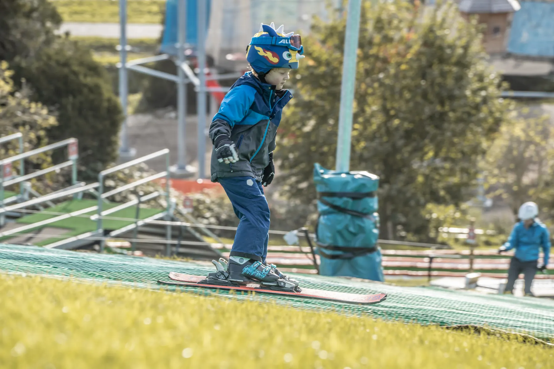 Een kind met helm skiet de piste af, met op de achtergrond de lift van de outdoor skibaan