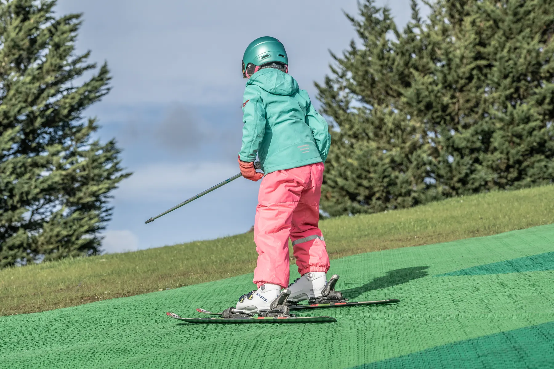 Een meisje met helm skiet over de groene skimatten van de outdoor skibaan